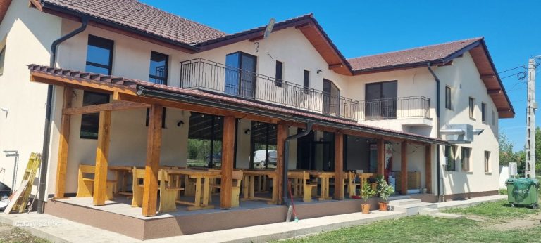 Terasa acoperită a Pensiunii Denis, cu mese și bănci din lemn masiv